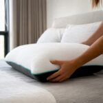 Una mano acomoda la almohada sobre una cama iluminada por la luz.